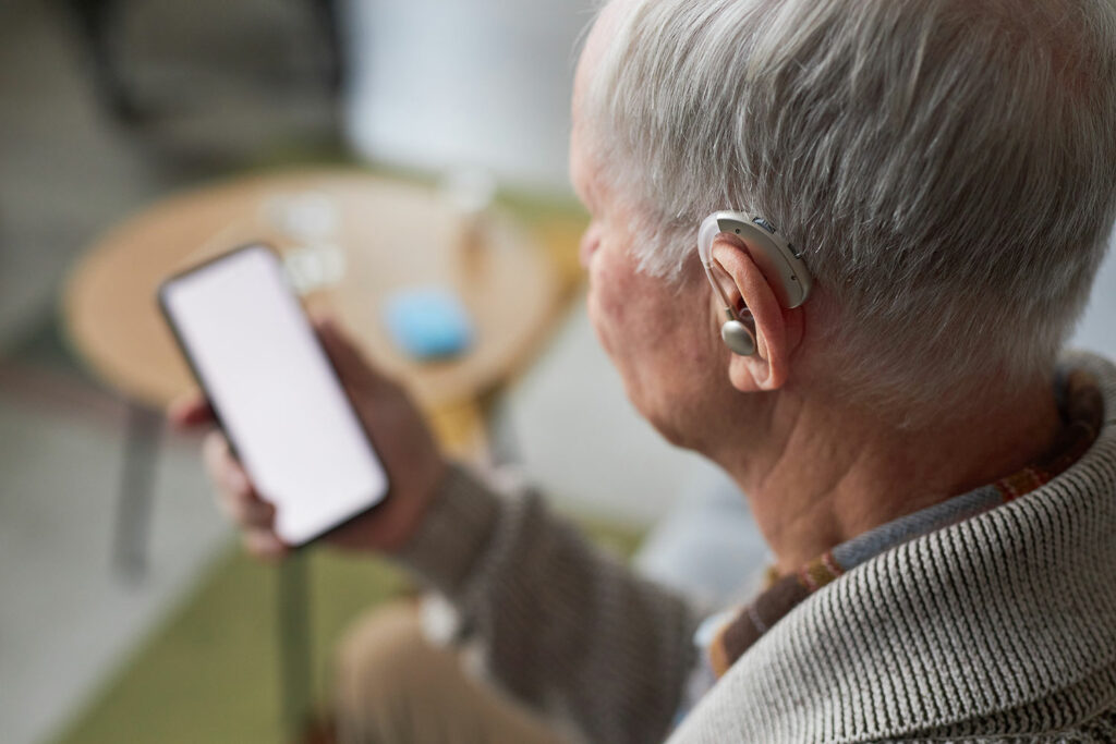 Mann mit Hörgerät und Smartphone